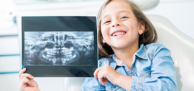 Child holding up digital x-ray of teeth and smiling to mirror the image
