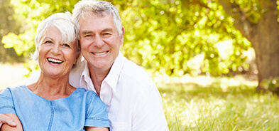 Older couple smiling outside to show off dental implants