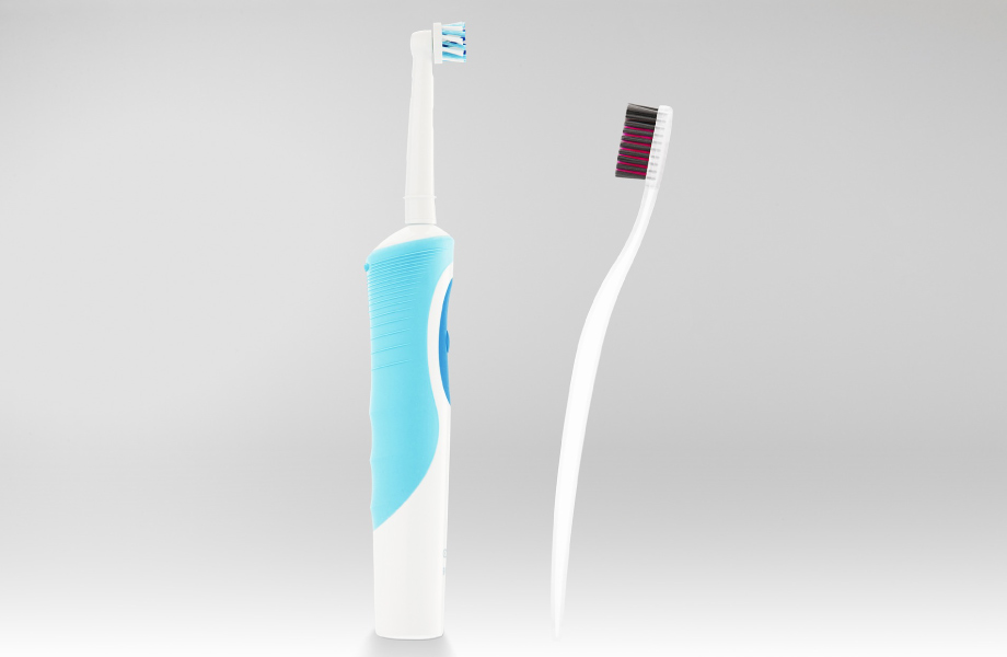 blue electric toothbrush next to white manual toothbrush with dark bristles against gray background