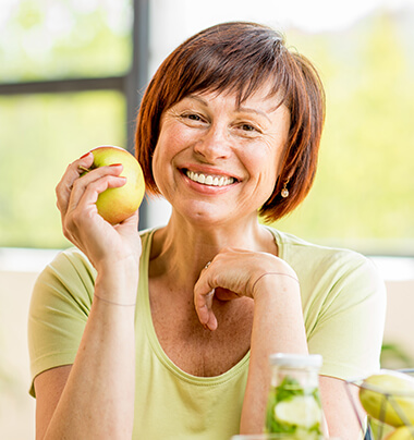 woman with dental crowns smiling as she holds an apple in her hand