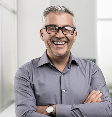 An older man with dental bridges smiling with his arms crossed