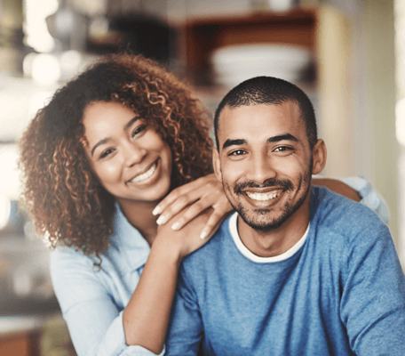 a young woman smiling as she rests her hands on her boyfriend's shoulder