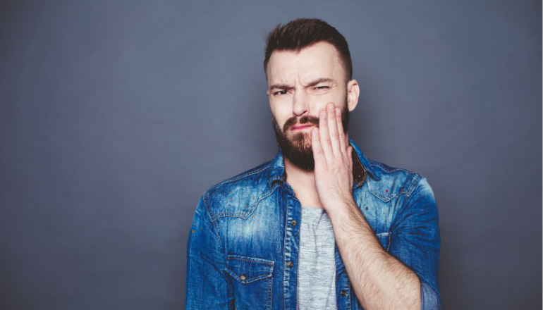 bearded man holds the side of his mouth with a dental emergency