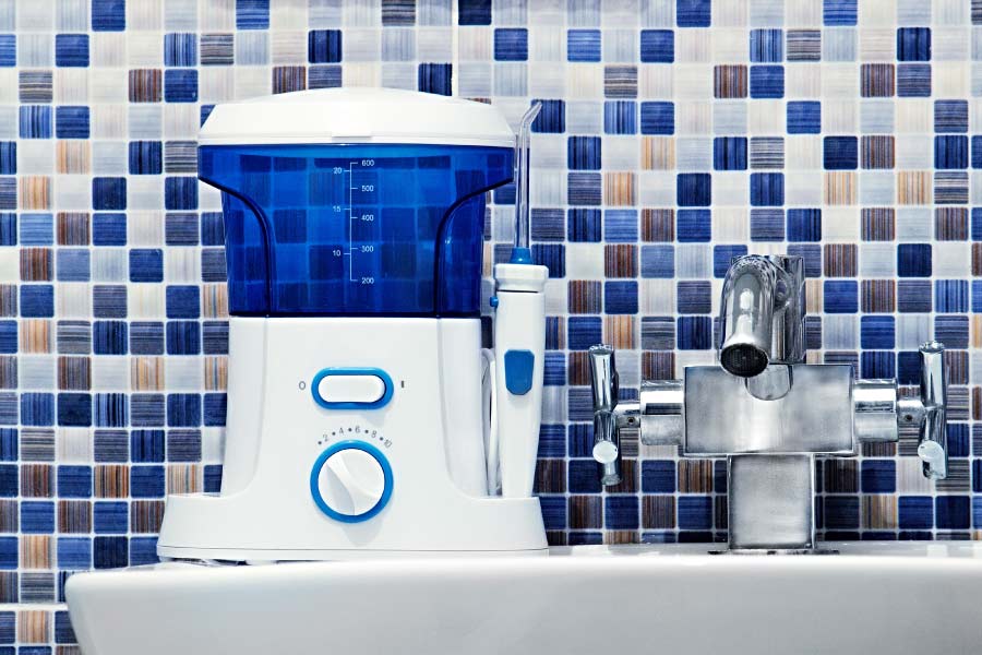 Water flosser on a sink in front of a blue mosaic tile backsplash