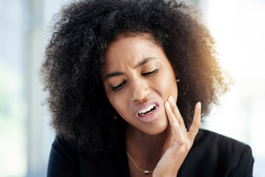 young woman holds her cheek in pain with a dental emergency