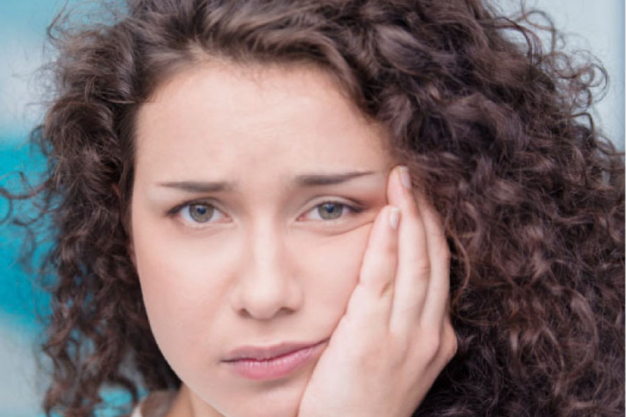 young woman holds her jaw in pain from wisdom teeth